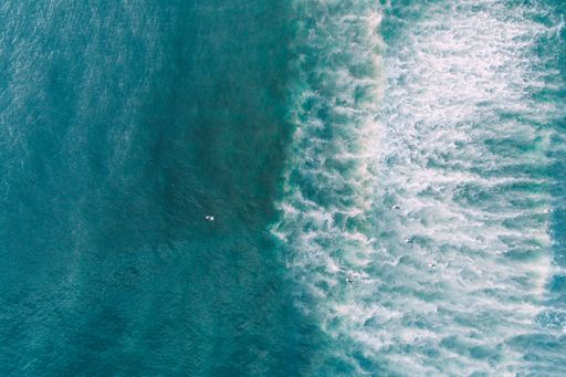 view of a wave on the shore of a beach at sunrise, and people surfing. Aerial zenithal view photography with a drone.