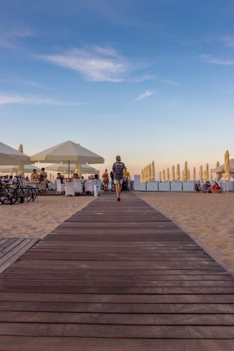 A vertical shot of a wooden pathway to a cafe with canopies on a sandy beach in Sopot, Poland