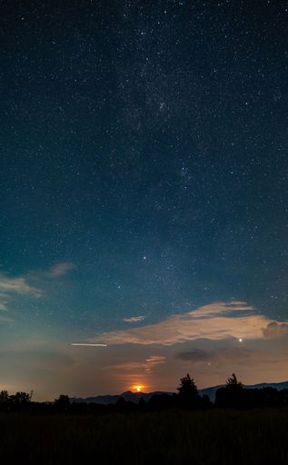Starry night sky over a silhouette of mountains with a glowing sunset, creating a serene and tranquil scene.