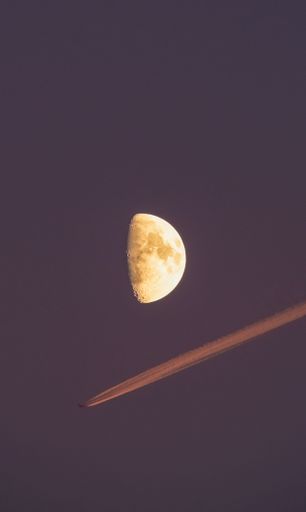 A striking image of a half moon with a jet contrail crossing the night sky, creating a dynamic composition.