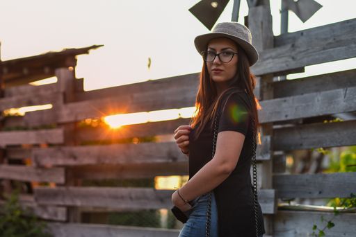 A vertical shot of a multi-racial lady from Serbia posing in front of a wooden fence during a scenic sunset