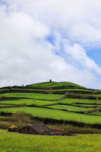 Scenic view of lush green terraced fields and a small house under a partly cloudy sky, showcasing rural beauty.