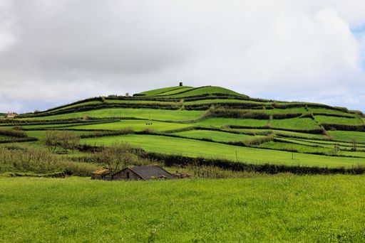 Lush green terraced hills under a cloudy sky in a rural landscape, showcasing natural beauty and agricultural design.