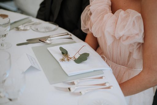 A closeup shot of a female wearing a dress sitting in front of a wedding table with a napkin and green leaf on it