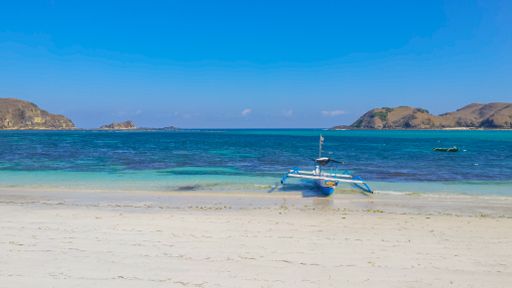 Beautiful paradise lagoon beach background with white sand, blue water and clear sky and a small longtail boat at Tanjung An on Lombok in Indonesia.