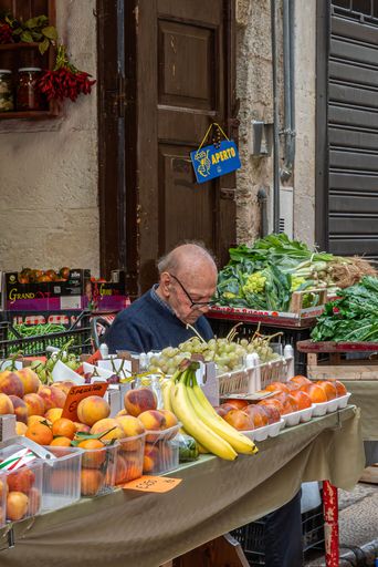 An Italian vendor sells vegetables at a stand in a narrow alley in Bari's historic old town.