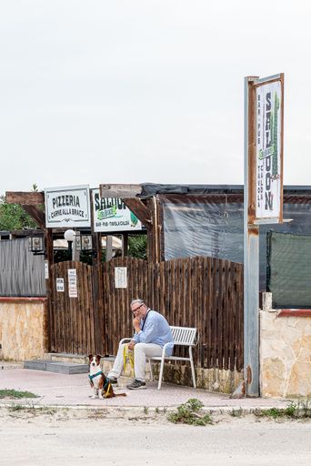 An elderly man with a dog on a bench in a quiet Italian town