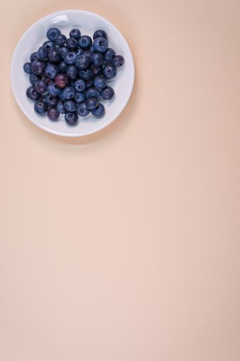 A vertical closeup of a white plate with blueberry on the peach background.