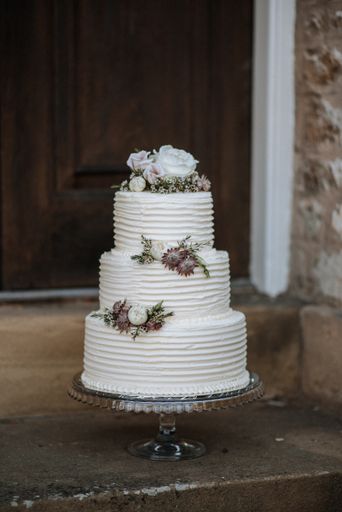 A vertical shot of a three-layer wedding cake decorated with flowers on a silver platter