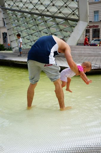 A young father playing with his child in a fountain at the Wolnosci square
