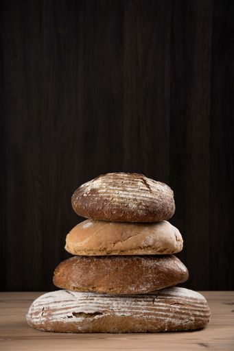 A stack of artisanal bread loaves on a wooden table with a dark wooden background.