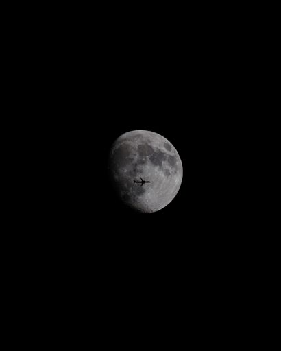 Airplane silhouette crossing the moon in a dark night sky