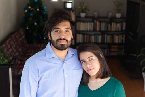 A cheerful young Hispanic couple or friends looking at the camera in a living room