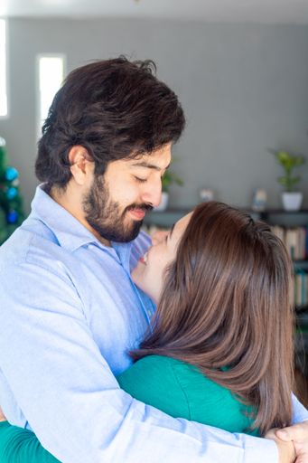A vertical shot of a cheerful young Hispanic couple hugging and looking  each other indoors