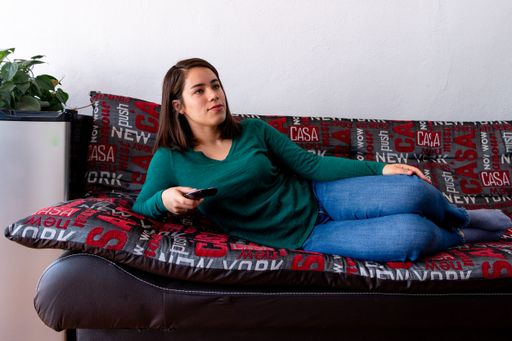 A young Hispanic lady lying on the couch holding a remote control