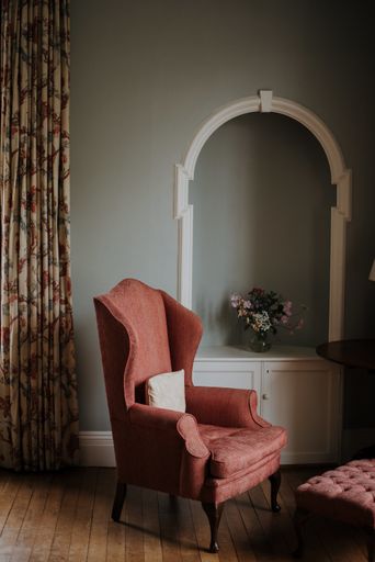A vertical shot of a red armchair, a white stand with a flower on it in a room