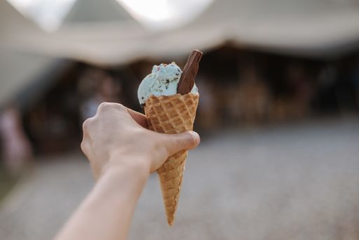 A closeup shot of a person holding an ice cream cone with blue flavored ice cream ball with a chocolate slice