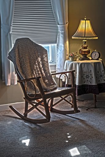 Cozy interior with a rocking chair draped in a blanket beside a lamp-lit table, creating a warm and inviting atmosphere.