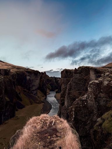 Dramatic view of Feather River Canyon with rugged cliffs and a winding river under a partly cloudy sky at sunset.