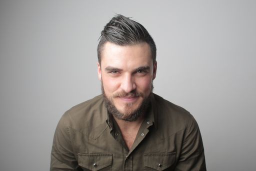 A closeup shot of a Caucasian man from Hungary smiling at the camera in front of a gray background