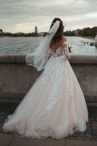 A vertical full body shot of a bride wearing  white gown and wedding dress standing on a bridge