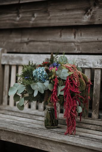 A vertical shot of a flower bouquet in a glass vase on a wooden bench