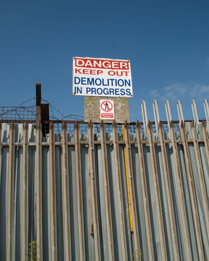 Warning sign above an old metal palisade fence with some barbed wire, Tranmere, Merseyside.
