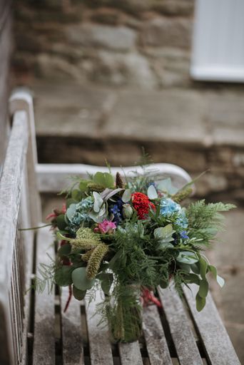 A vertical shot of a flower bouquet in a glass vase on a wooden bench