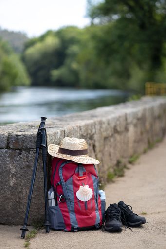 A Backpack and other gear of a pilgrim to Santiago de Compostela leaning against a stone wall. Camino de Santiago concept. Copy space