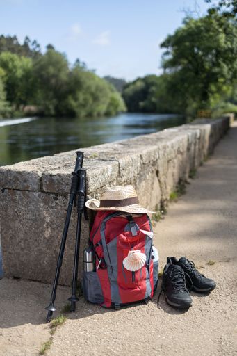 A Backpack and other gear of a pilgrim to Santiago de Compostela leaning against a stone wall. Camino de Santiago concept. Copy space