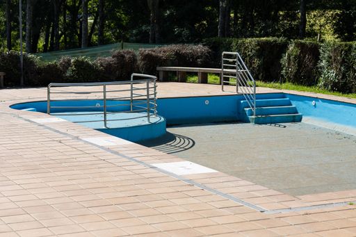 An empty swimming pool with faded paint and overgrown surroundings hints at a bygone era.