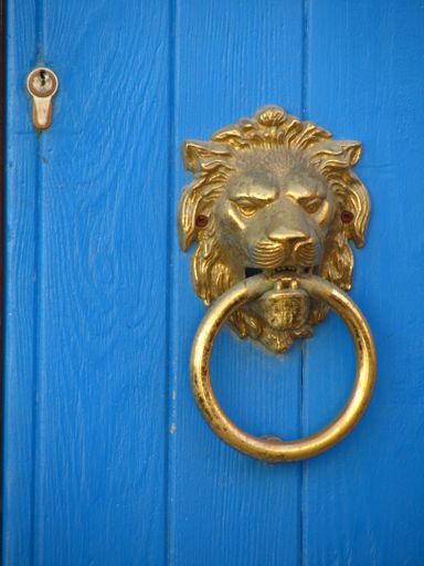 A closeup of a traditional lion head-shaped golden ring on the wooden blue door in Zurrieq, Malta