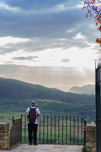 A tourist with hat and backpack, not recognizable, leaning out of a balcony looking at the landscape