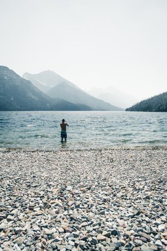 A vertical shot of a man standing in the water near the shore.