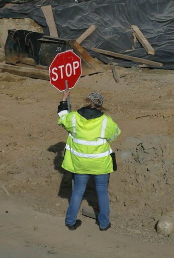 A back view of a female construction worker holding the metal "STOP" sign