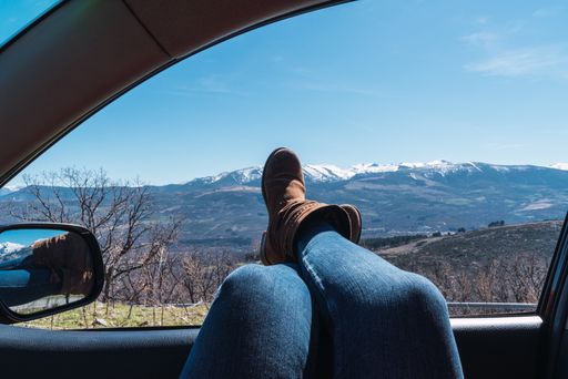 A female's feet sticking out of car window with a beautiful view of mountains under a clear sky