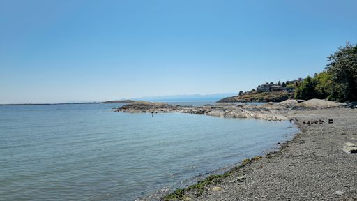 Scenic view of a rocky coastline with clear blue skies and calm waters, featuring a distant house on a hill.