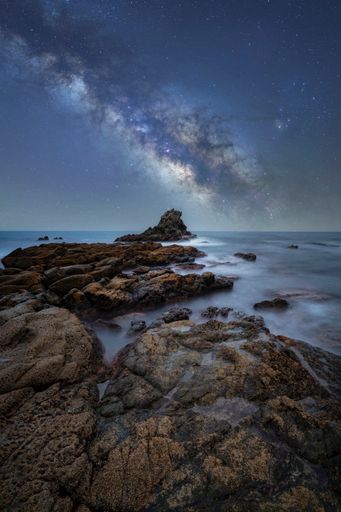 A vertical shot of an ocean and rocks under the magical skies