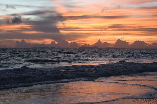 Dramatic sunset over a tranquil ocean with vibrant clouds reflecting on the water's surface.