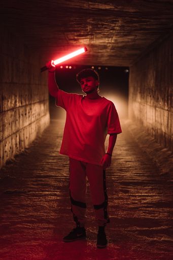 A young attractive Spanish man with oversized clothes holding a red light in an underground building