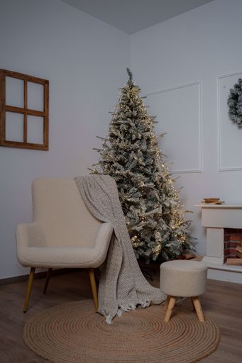 A cozy living room with a decorated Christmas tree, armchair, and stool, creating a holiday atmosphere