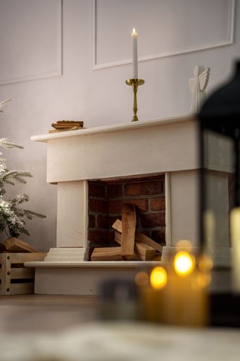 A cozy interior with a candlelit mantelpiece and stacked firewood in a brick fireplace