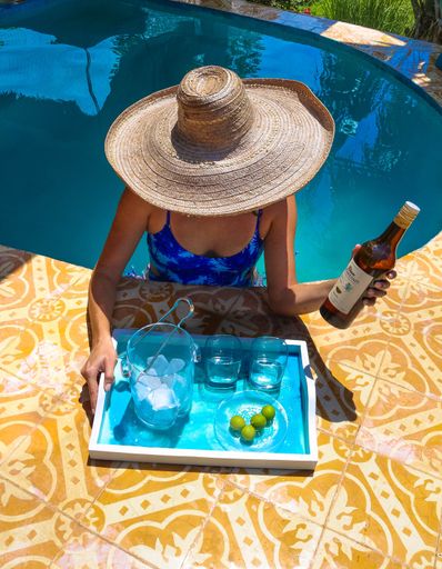 A summertime shot of a female holding a drink in front of a tray with ice and glasses in a pool