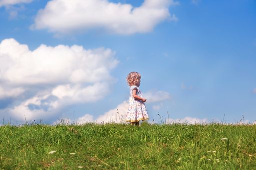 A beautiful shot of a caucasian baby in a dress standing in the middle of a field