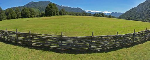 The mesmerizing view of the wooden fence in the field with the trees and mountains in the background