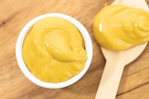 A Top view of Mustard sauce in bowl and spoon on wooden table