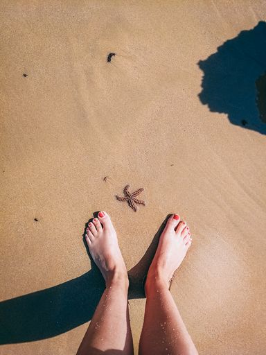 A top view of a starfish and female feet with red pedicure on the sand of the Olhos de Agua beach