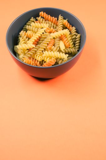 A vertical shot of tri-color rotini pasta on a bowl isolated on an orange background