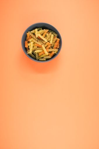 A vertical shot of tri-color rotini pasta on a bowl isolated on an orange background