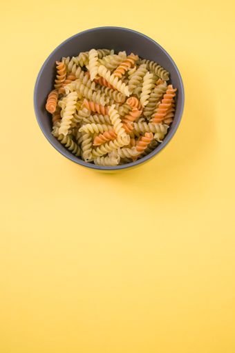 A vertical shot of tri-color rotini pasta on a bowl isolated on yellow background